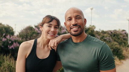 A multi-ethnic couple of young people standing together and smiling, male and female athletes against trees and sky background, sporty people diverse. Сouple goals and motivation