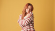 © Andrii Nekrasov - Cute red-haired woman dressed in sweater hugs herself looking at camera on yellow background. Beautiful girl poses in studio with blank space on yellow wall for your promotion