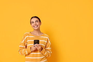 Wall Mural - Smiling woman with smartphone on yellow background. Space for text