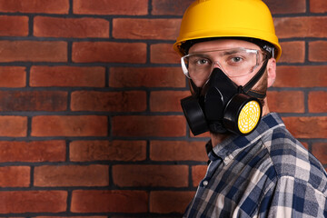 Wall Mural - Man in respirator mask and hard hat near red brick wall. Space for text