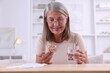 © New Africa - Senior woman with pills and glass of water at table indoors