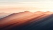 © Dulemegapixel - The photograph captures the golden hues of dawn light softly cascading over a series of mountain peaks, creating a warm and tranquil scene reminiscent of a dreamscape.