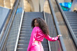 © @skuder_photographer - A beautiful young Latin woman with big brown eyes and long curly hair wearing a pink skirt and jacket and high heels walks up the escalator. The woman is a very elegant and empowered executive.