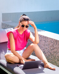 Wall Mural - Happy woman sitting at pool and using her laptop