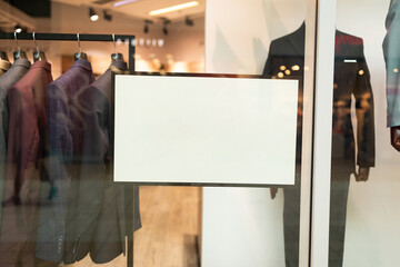 White paper poster mockup displayed inside a clothing store window. Marketing and business concept.