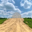 © Atlas - Construction workers inspecting a large geometric structure under a bright sky