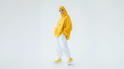 a young asian woman in a yellow hijab, smiling softly as she poses against a white background, exudi