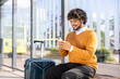 © Liubomir - Smiling man sitting at bus stop using smartphone with suitcase beside him. Sunny day setting highlighting casual travel and connectivity. Ideal for travel, transportation, communication themes.