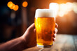 © JEROSenneGs - Hand holding beer mug in bar, with blurred background.