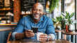 © Carmen - Older African-American man smiling and looking at smartphone, while updating his social media in a cafe