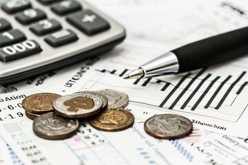 A calculator, pen, and coins are on top of a piece of paper with graphs