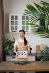 Wall Mural - Woman in apron holding box of cupcakes in kitchen