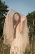 © Milou Dirks - asian young woman in a dress on summer evening sunset in field holding fabric
