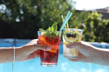 Poster - Women holding tasty cocktail in glass near swimming pool outdoors, closeup