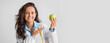© Prostock-studio - A nutritionist wearing a lab coat smiles while holding a green apple in her hand. She gestures invitingly, sharing important tips about healthy eating habits and nutrition, copy space
