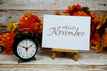 Canvas Print - Hello November text with alarm clock and maple leaf decoration on wooden background