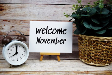 Wall Mural - Welcome November text on paper card with alarm clock on wooden background