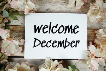 Wall Mural - Welcome December text on paper card with flowers frame top view on wooden background