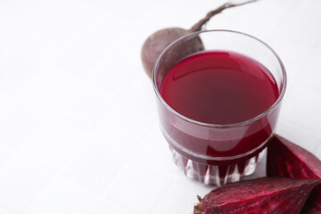 Wall Mural - Fresh beet juice in glass and ripe vegetables on white tiled table, closeup. Space for text