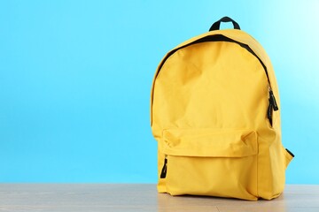 Wall Mural - Yellow backpack on wooden table against light blue background, space for text