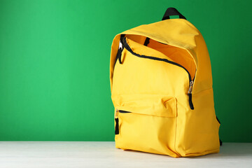 Poster - One yellow backpack on white table against green background, space for text