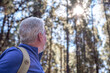 © luciano - Active white haired senior man with backpack enjoying a day hike in mountain forest looking at the sky. Healthy lifestyle for retired people