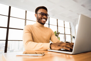 Poster - Coworking Concept. Happy african freelancer working on laptop in modern shared workplace. Copy space