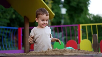 Wall Mural - Adorable joyful toddler tapping his hands by the sand. Lovely Caucasian kid playing in the sandbox outdoors.