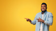 © Prostock-studio - Cool offer. Cheerful african american man pointing two fingers aside at copy space on yellow studio background, panorama