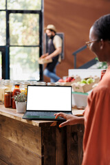 Female customer browsing on laptop with an isolated white screen. African american woman using minicomputer displaying blank chromakey mockup template in an eco friendly sustainable store.