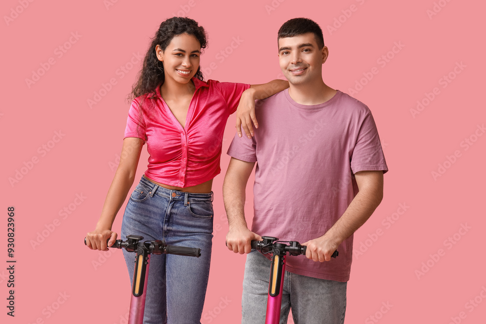Happy young couple with modern electric kick scooters on pink background