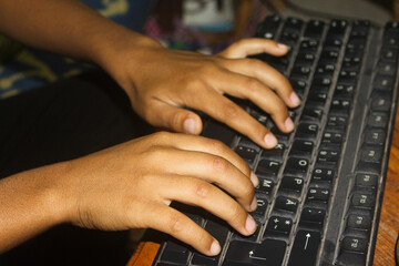 A person's hands are typing on a computer keyboard. The person appears to be wearing a black shirt with yellow writing on it.