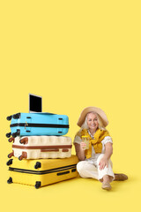 Sticker - Mature businesswoman with cocktail, laptop and suitcases ready for summer vacation on yellow background