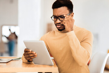 Poster - Reading News. Pensive black businessman in glasses using tablet checking his mail or schedule, free space