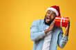 © Prostock-studio - Portrait of crazy black guy in Santa hat holding Christmas gift box, excited about what's inside, yellow studio background with free space