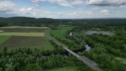 Wall Mural - aerial drone footage of cars driving on country rural road next to a power plant over a small bridge above rondout creek in kingston hudson valley new york and mountains in background