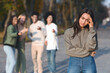 © Prostock-studio - Sad muslim girl staying aside from laughing international group of teenagers, park background