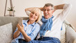 © Prostock-studio - Happy mature couple using cellphone, surfing internet online, sitting on sofa at home, free space