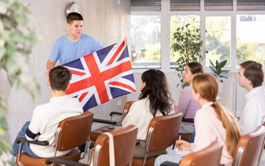 Young male teacher showing flag of united kingdom to group of students