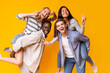 © Prostock-studio - Two mixed race teen couples having fun over yellow studio background, posing on camera, making piggy-back