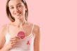 © Pixel-Shot - Young woman with pink ribbon and cookie on color background, closeup. Breast cancer awareness concept