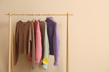 Rack with sweaters and autumn leaf near beige wall