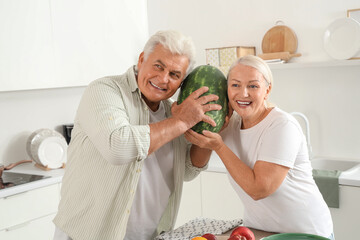 Wall Mural - Mature couple checking watermelon for ripeness in kitchen