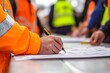 © Unic - Working at heights permit book placing on the table, defocused construction site supervisor reviewing job hazard analysis risk safety assessment prior approval and sign off work on open field