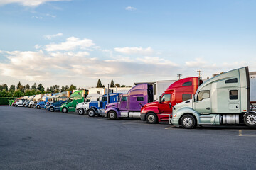 Wall Mural - Long row of the big rig semi trucks with semi trailers standing on the truck stop parking lot at twilight time