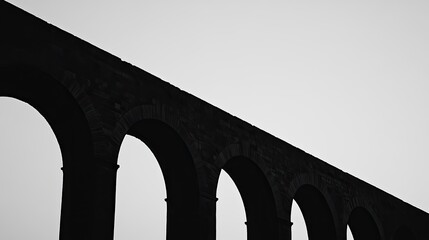 Minimalist view of a historic aqueduct, silhouetted against a clear sky, with the focus on its elegant arches and structure.