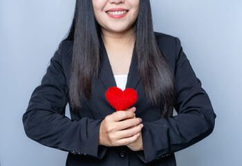 Asian woman wearing a black suit Smiling brightly holding a red heart. How to take care of your health Symbols about love, medical concept, heart disease and insurance concepts, Valentine's Day 