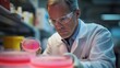 © Charoen - Scientist in a lab coat examining a petri dish with bacteria cultures, focusing on pharmaceutical research and development.