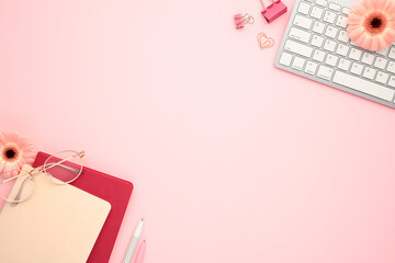Wall Mural - Modern workspace in a home office with keyboard, paper notebooks, eyeglasses, flowers on pastel pink background.