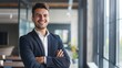 © JINGWEN - Smiling handsome businessman with crossed arms in modern office, young man exuding confidence, business success concept.